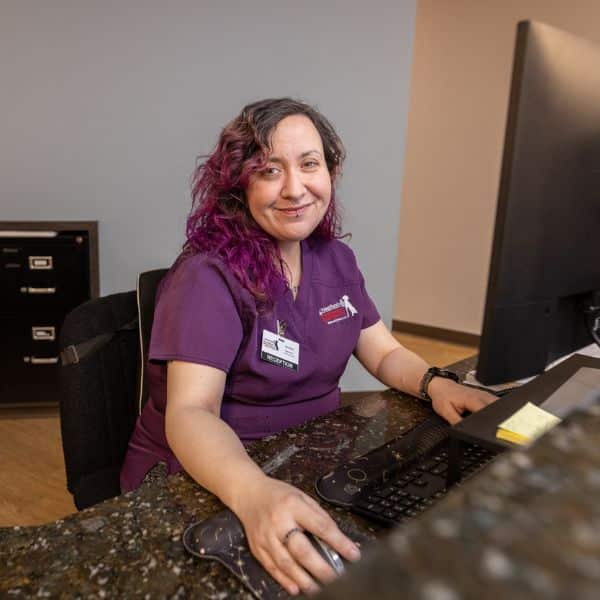 A woman in a purple shirt sits at a desk